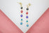 A pair of gold dangle earrings showcases a colorful stack of evil eye charms in black, red, royal blue, turquoise, and light blue.
