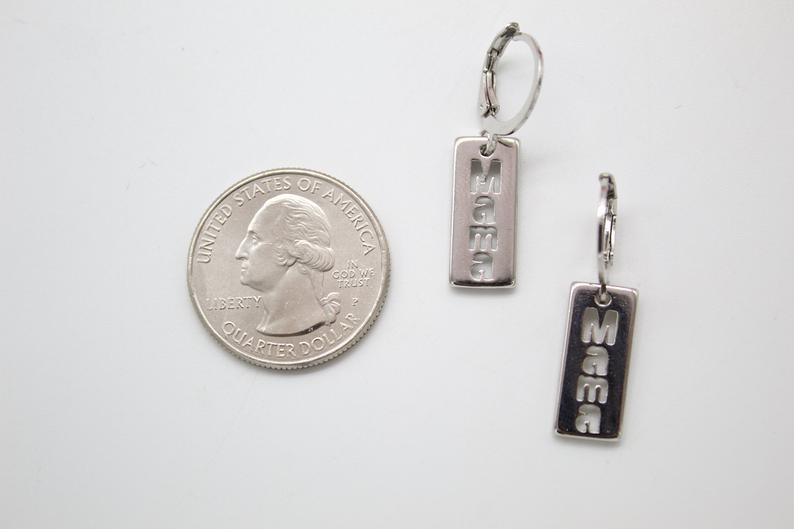 A pair of silver "Mama" drop earrings sits next to a US quarter coin for scale.