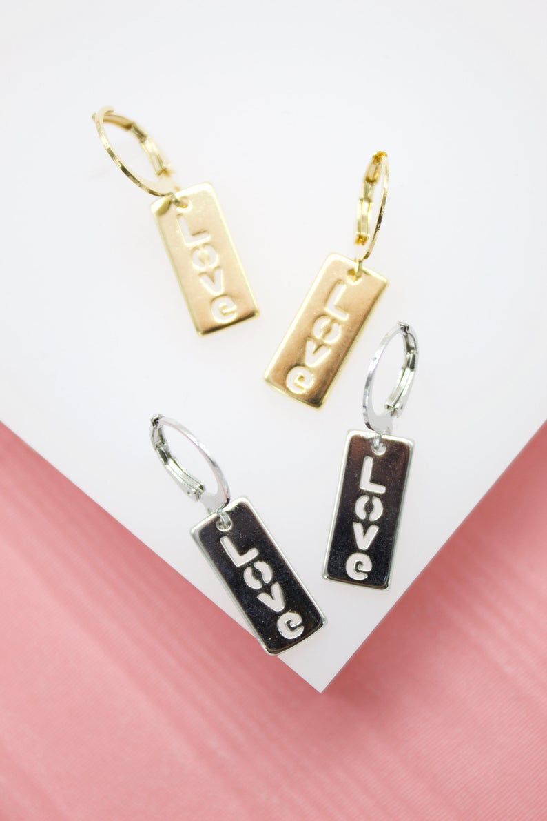 Two pairs of gold and silver rectangle hoop earrings featuring the word "love" cut out display on a white surface.