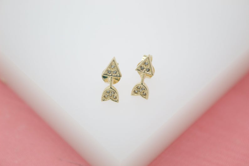 A pair of dainty gold arrow stud earrings sparkle on a white display surface.