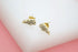 A pair of gold croissant stud earrings sparkle against a soft pink and white background.