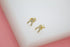 A pair of gold wishbone stud earrings encrusted with sparkling cubic zirconia stones rests on a white display block.