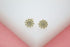 A pair of sparkling gold sunburst stud earrings encrusted with tiny cubic zirconia stones rests on a white display surface.