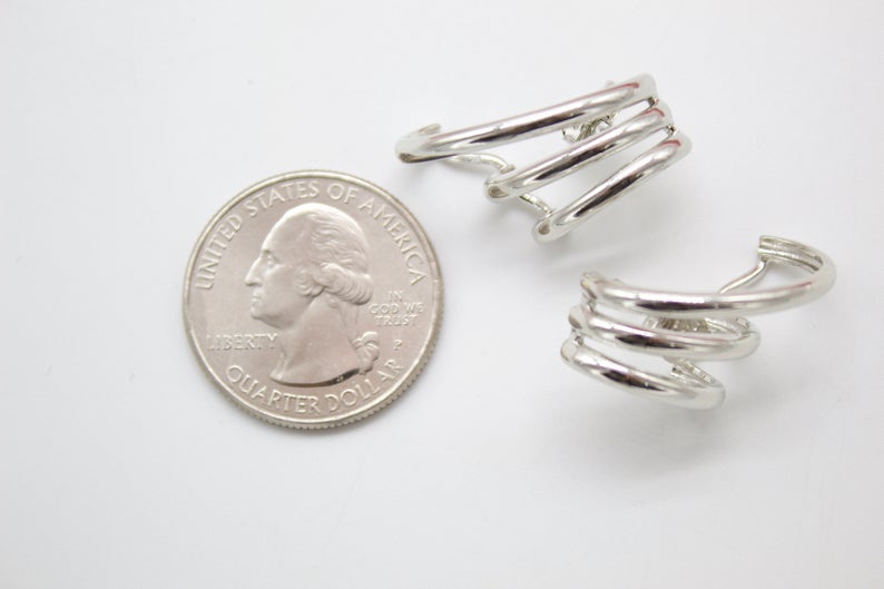 A pair of modern multi-strand silver hoop earrings rests next to a US quarter on a white surface to show their scale.