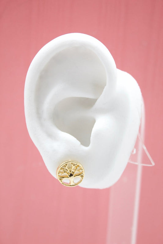 A white mannequin ear displays a round gold tree-of-life stud earring against a pink background.