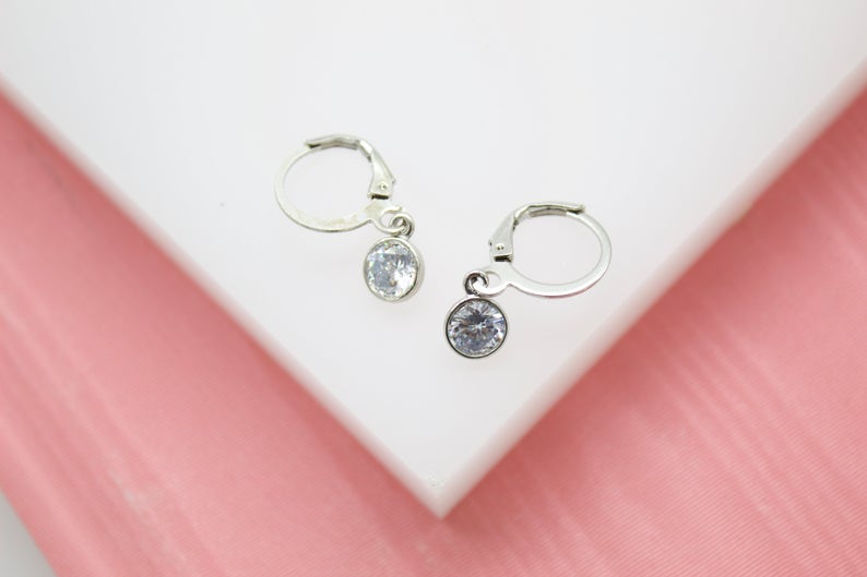 A pair of silver leverback earrings with dangling cubic zirconia stones rests on a white display surface.