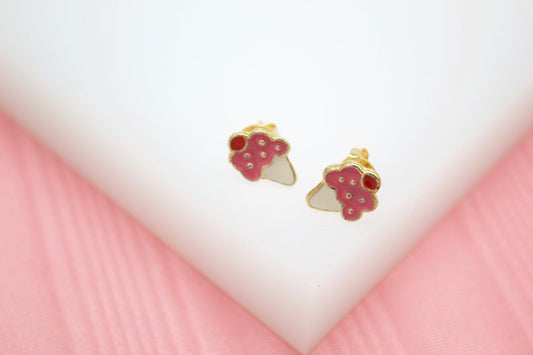 A pair of gold-plated ice cream cone stud earrings featuring pink enamel and red cherries rests on a white display surface.