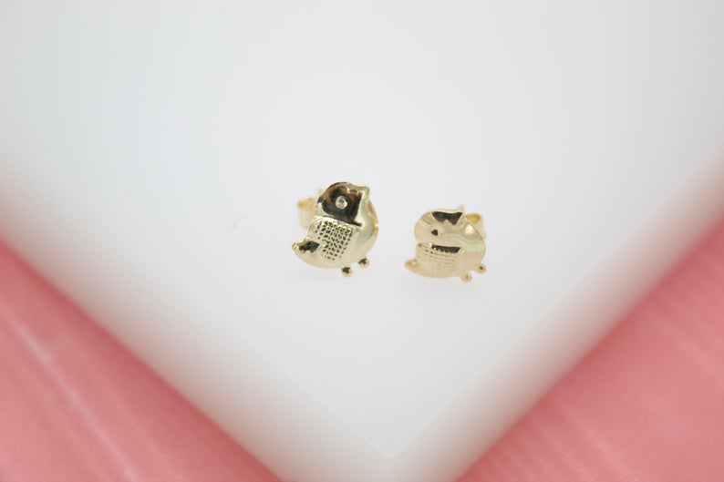 A pair of cute gold bird stud earrings resting on a white display surface.