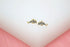 A pair of gold dolphin stud earrings features sparkling cubic zirconia pave details against a white and pink background.