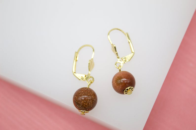 A pair of gold leverback earrings features dangling brown sandstone spherical beads.