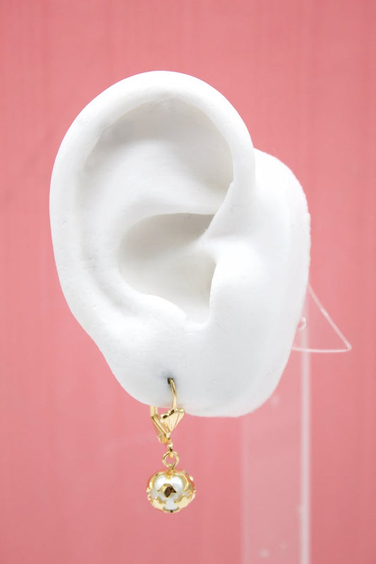 A white model ear displays a gold leverback earring featuring a pearl and star cage charm against a pink background.