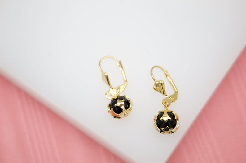 A pair of elegant gold leverback earrings features hanging black spheres cradled in intricate cut-out designs.
