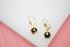 A pair of elegant gold leverback earrings features hanging black spheres cradled in intricate cut-out designs.