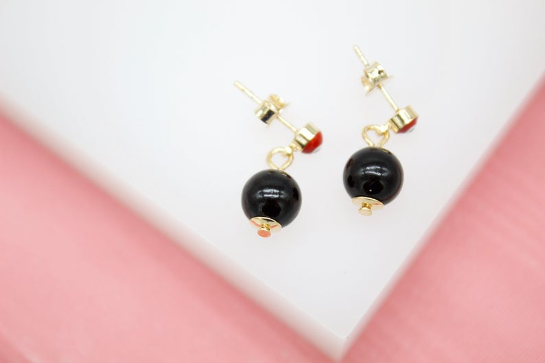 A pair of elegant gold earrings featuring dangling black spherical beads rests on a white display surface.