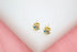 A pair of gold turtle stud earrings featuring colorful enamel details sits on a white display surface against a soft pink background.