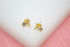 A pair of gold elephant stud earrings featuring sparkling cubic zirconia stones rests on a white display surface against a soft pink background.