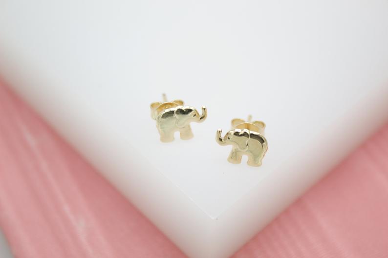 A pair of charming gold elephant stud earrings rests on a white display surface.
