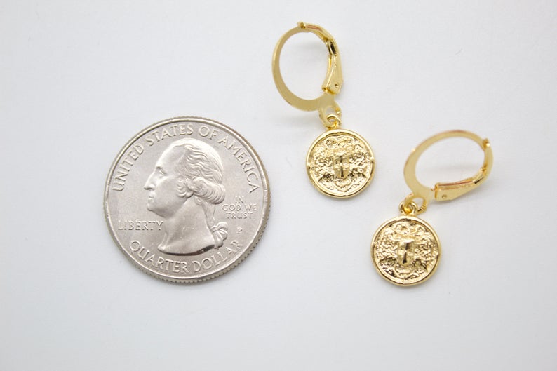 Two gold coin dangle earrings rest next to a US quarter for size comparison on a white surface.