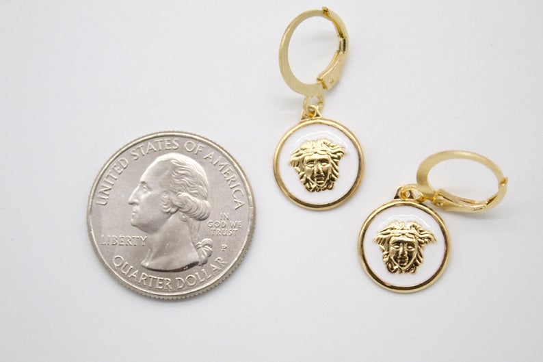 A pair of gold-plated Medusa head enamel earrings rests next to a US quarter coin for scale.