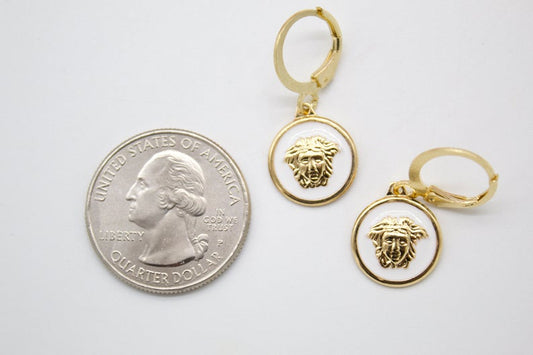 A pair of gold-plated Medusa head enamel earrings rests next to a US quarter coin for scale.
