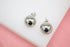 A pair of polished silver ball stud earrings rests against a white and pink backdrop.