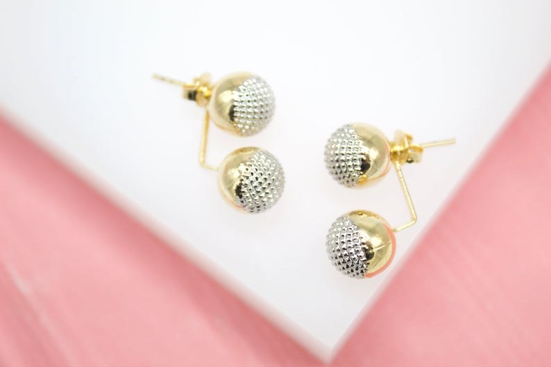 A pair of gold double ball stud earrings resting on a white display surface.
