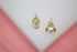 A pair of gold wire-wrapped pearl stud earrings rests on a white display stand against a soft pink background.