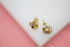 A pair of intricately intertwined tri-color gold hoop stud earrings rest on a white display surface.