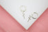 A pair of silver cross huggie hoop earrings rests on a white display against a soft pink background.