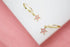 A pair of gold huggie hoop earrings featuring dangling pink enamel star charms with central cubic zirconia stones rests on a white display surface.