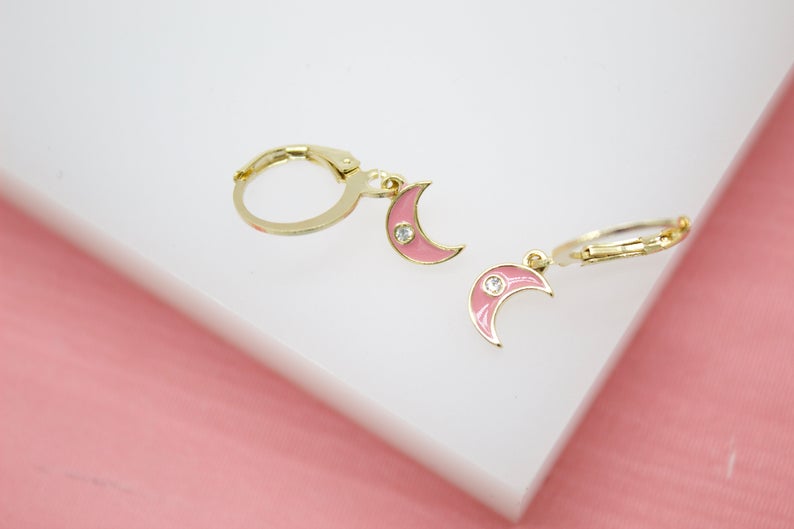 A pair of gold huggie hoop earrings features hanging pink enamel crescent moon charms accented with sparkling CZ stones.