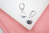 A pair of silver leverback earrings with engraved heart charms rests on a white surface against a pink background.