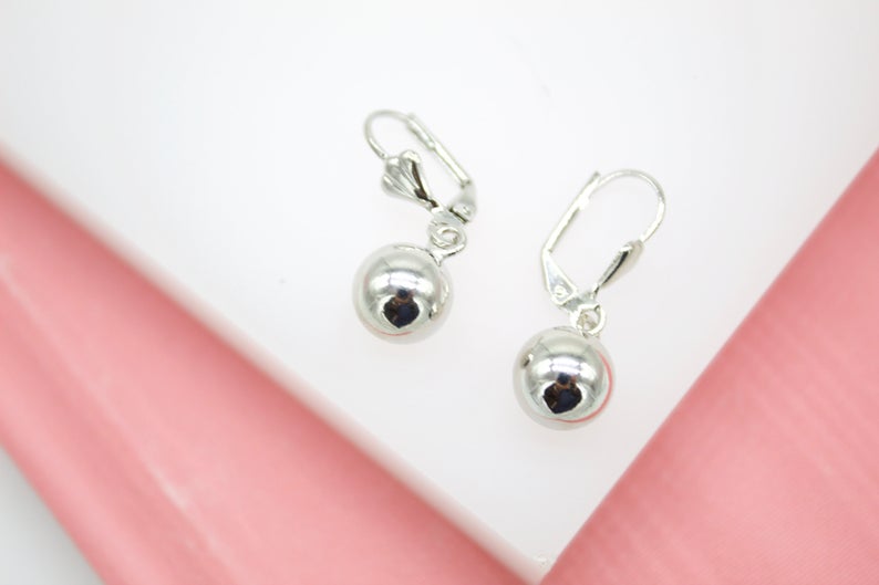 A pair of shiny silver ball drop earrings rests on a white and pink surface.
