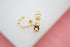 A pair of shiny gold chain link stud earrings rests on a clean white surface against a soft pink background.