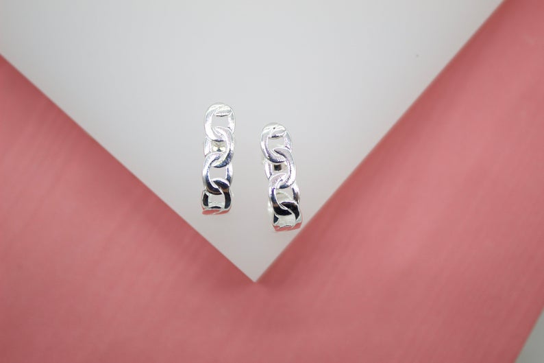 A pair of silver chain link hoop earrings rests against a white and pink display.