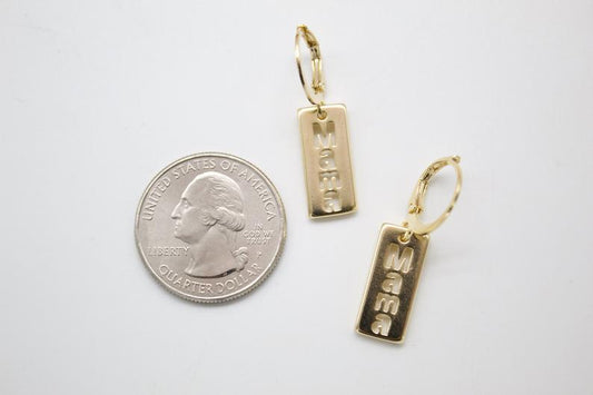 A pair of gold MAMA rectangle dangle earrings lies next to a US quarter coin for scale on a white surface.