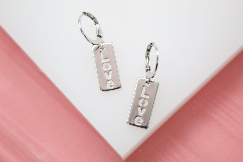 A pair of silver hoop earrings features rectangular dangles engraved with the word "LOVE".