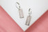 A pair of silver hoop earrings features rectangular dangles engraved with the word "LOVE".