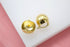 A pair of polished gold dome huggie earrings rests on a white and pink surface.