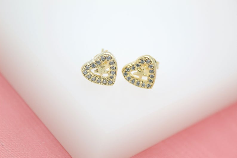 A pair of gold heart-shaped stud earrings features sparkling pave crystals and a cutout star detail in the center.