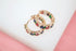 A pair of gold huggie hoop earrings featuring multicolored gemstones rests on a white and pink surface.