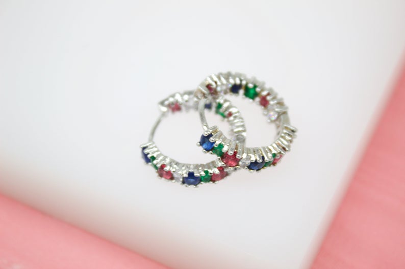 A pair of sterling silver hoop earrings with colorful multi-gemstones rest on a white surface.