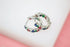 A pair of sterling silver hoop earrings with colorful multi-gemstones rest on a white surface.