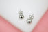 A pair of polished silver ball stud earrings rests against a white and pink background.