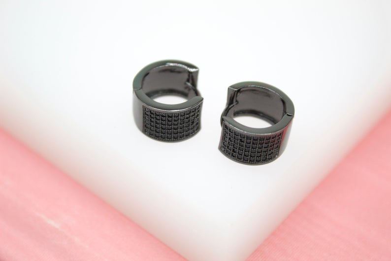 A pair of sleek black pave huggie earrings rests on a white display surface.
