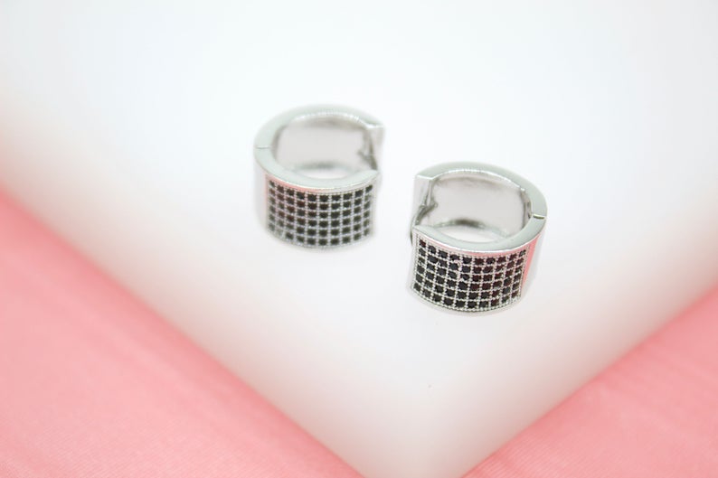 A pair of silver hoop earrings embedded with small black stones rests on a white display surface.