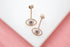 A pair of rose gold evil eye drop earrings embellished with sparkling white diamonds and deep blue sapphire centers rests on a white surface.