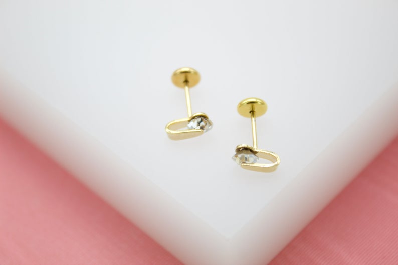 A pair of dainty gold stud earrings featuring delicate crystal stones rest on a white surface.