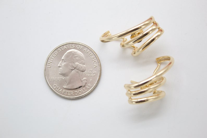 Two gold triple-band hoop earrings lie next to a US quarter coin on a white surface for size comparison.