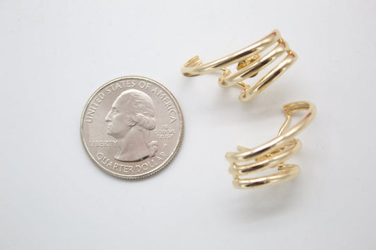 Two gold triple-band hoop earrings lie next to a US quarter coin on a white surface for size comparison.
